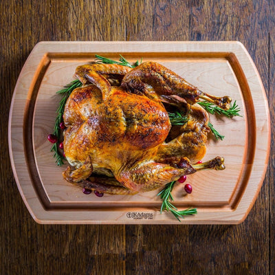 Roasted turkey with a golden-brown skin on a wooden cutting board, garnished with sprigs of rosemary and a few cranberries.