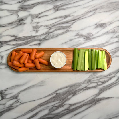 Wooden platter with carrots, celery, and a small bowl of dip on a marble surface