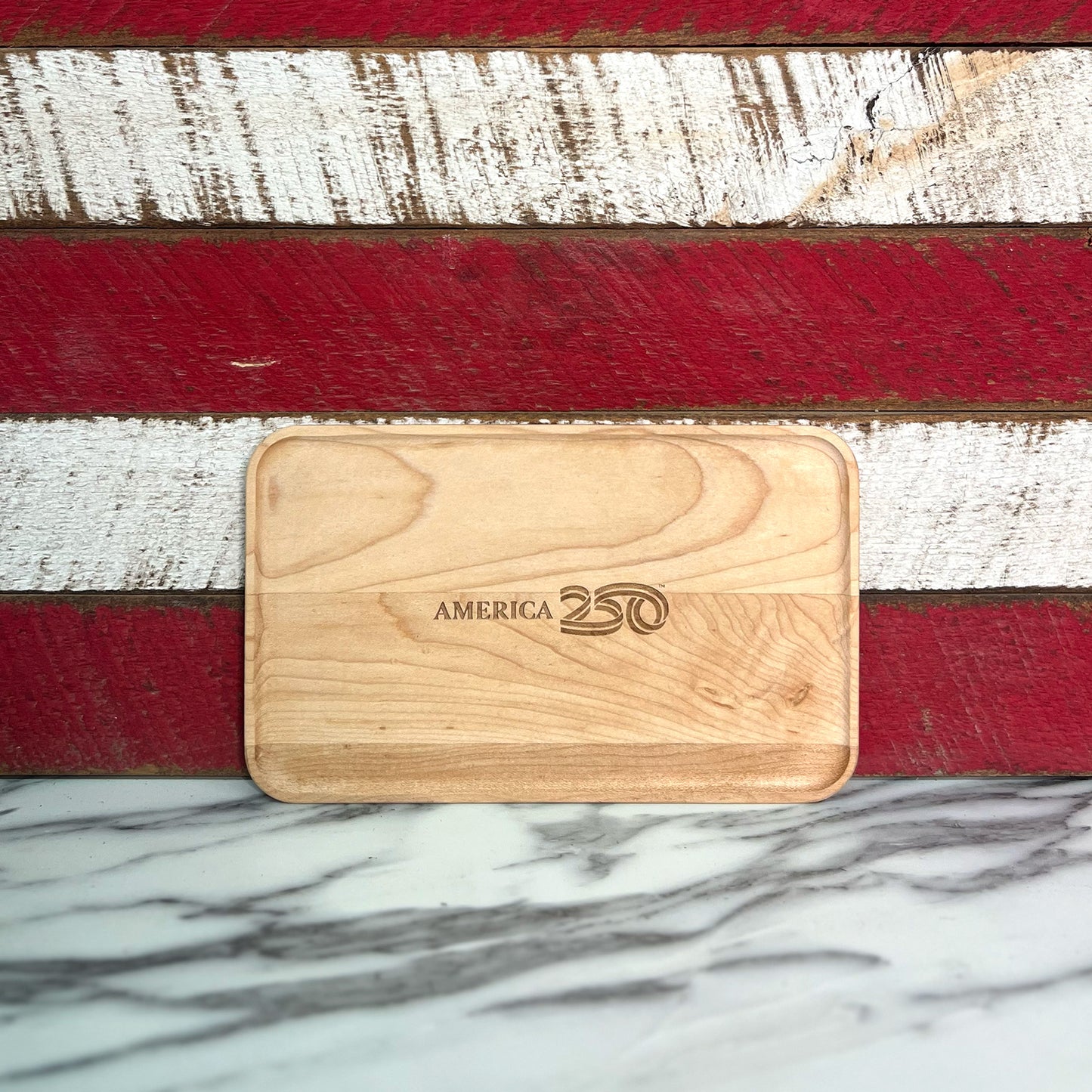 Wooden cutting board with 'America 250' branding on a red, white, and blue striped background.