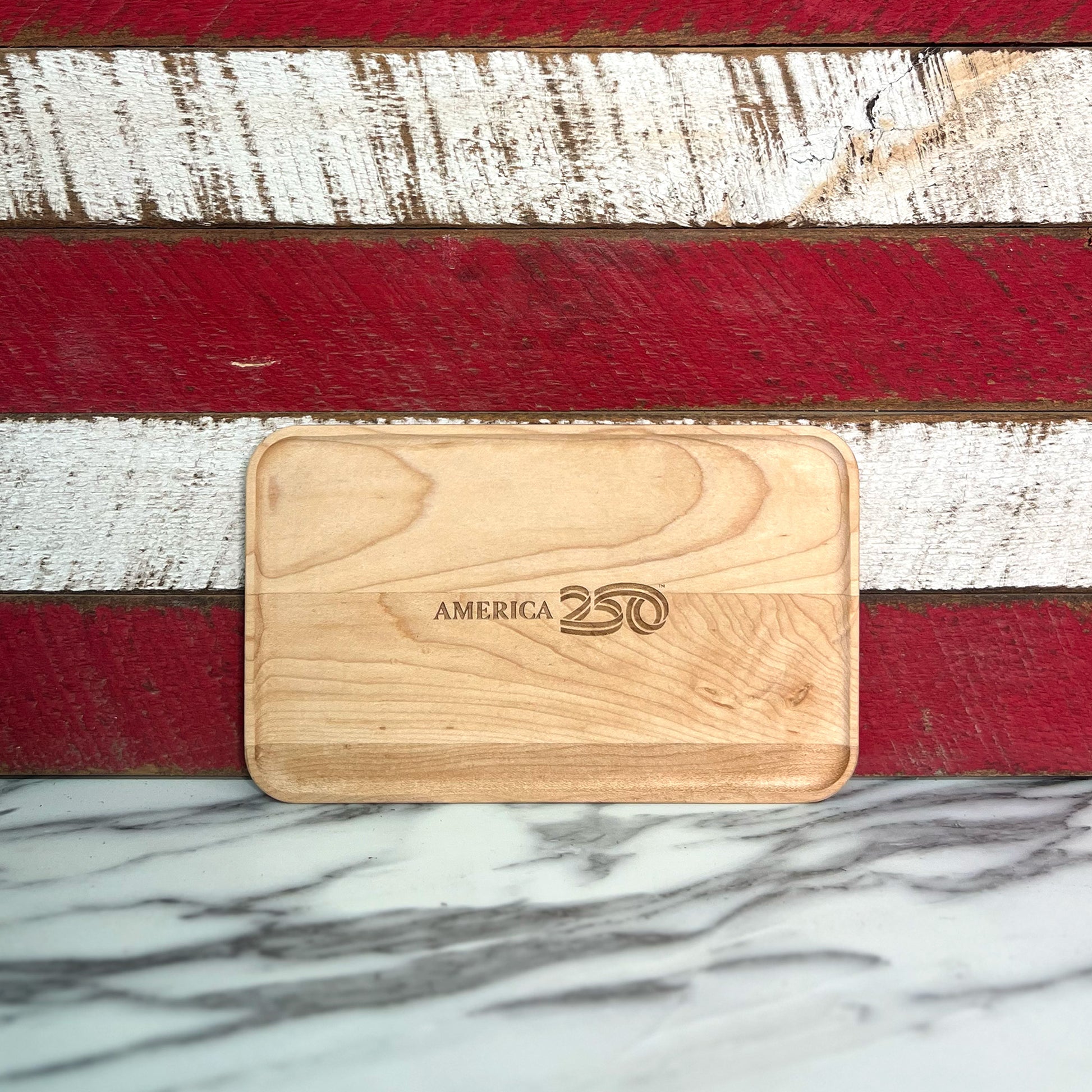 Wooden cutting board with 'America 250' branding on a red, white, and blue striped background.