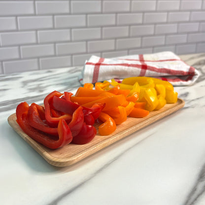 Sliced red and yellow bell peppers on a wooden board with a kitchen towel in the background.
