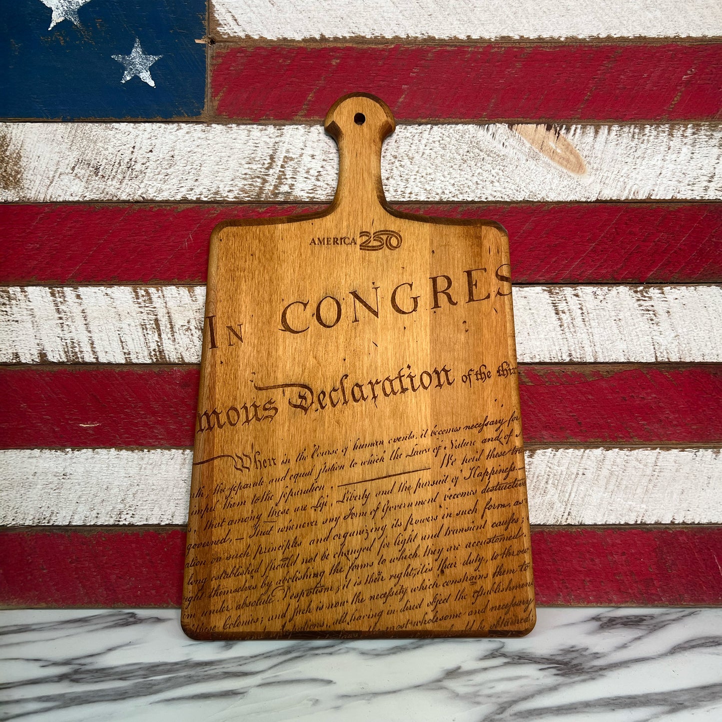 Wooden cutting board with engraved text on an American flag background.