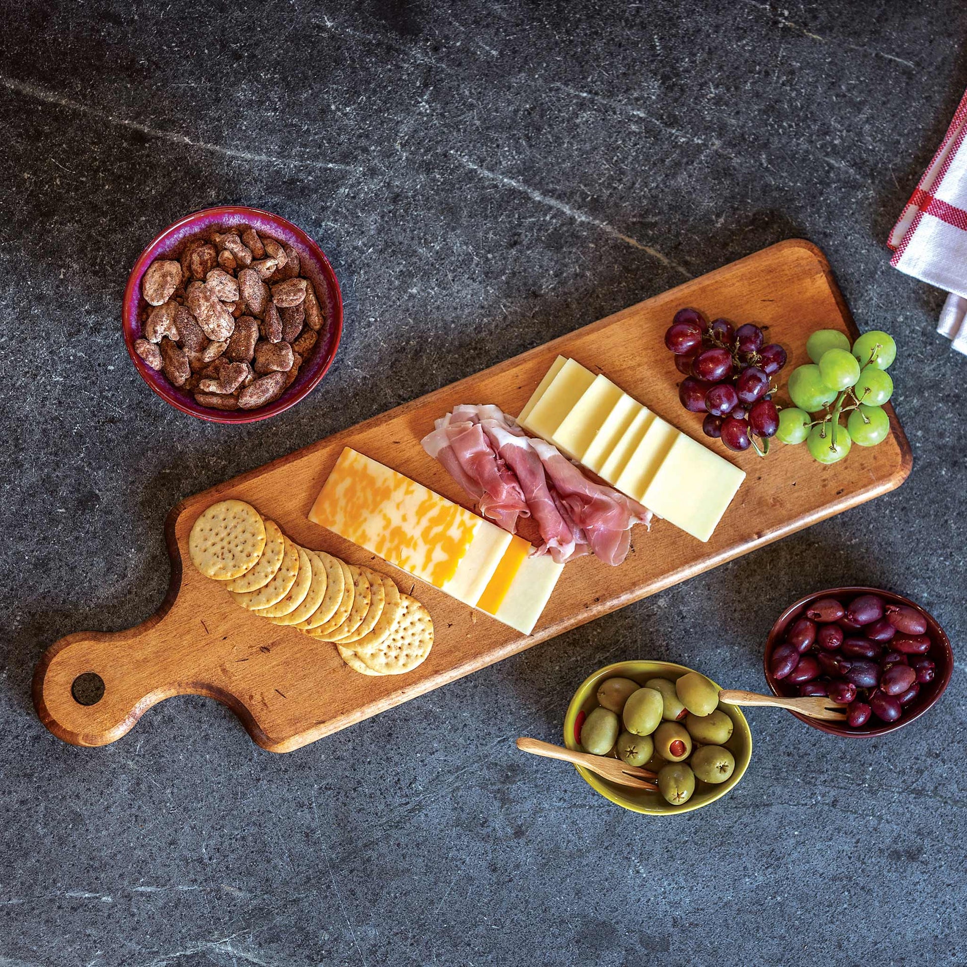 Wooden charcuterie board with cheese, meats, crackers, and fruits on a dark surface.