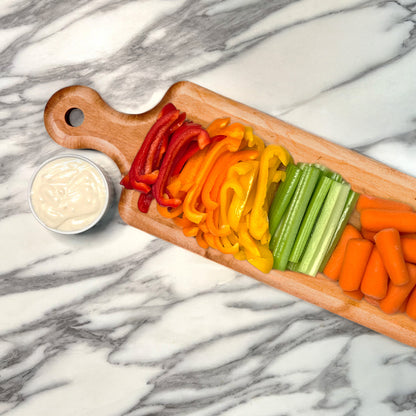 Wooden cutting board with sliced bell peppers, celery, and carrots on a marble surface.