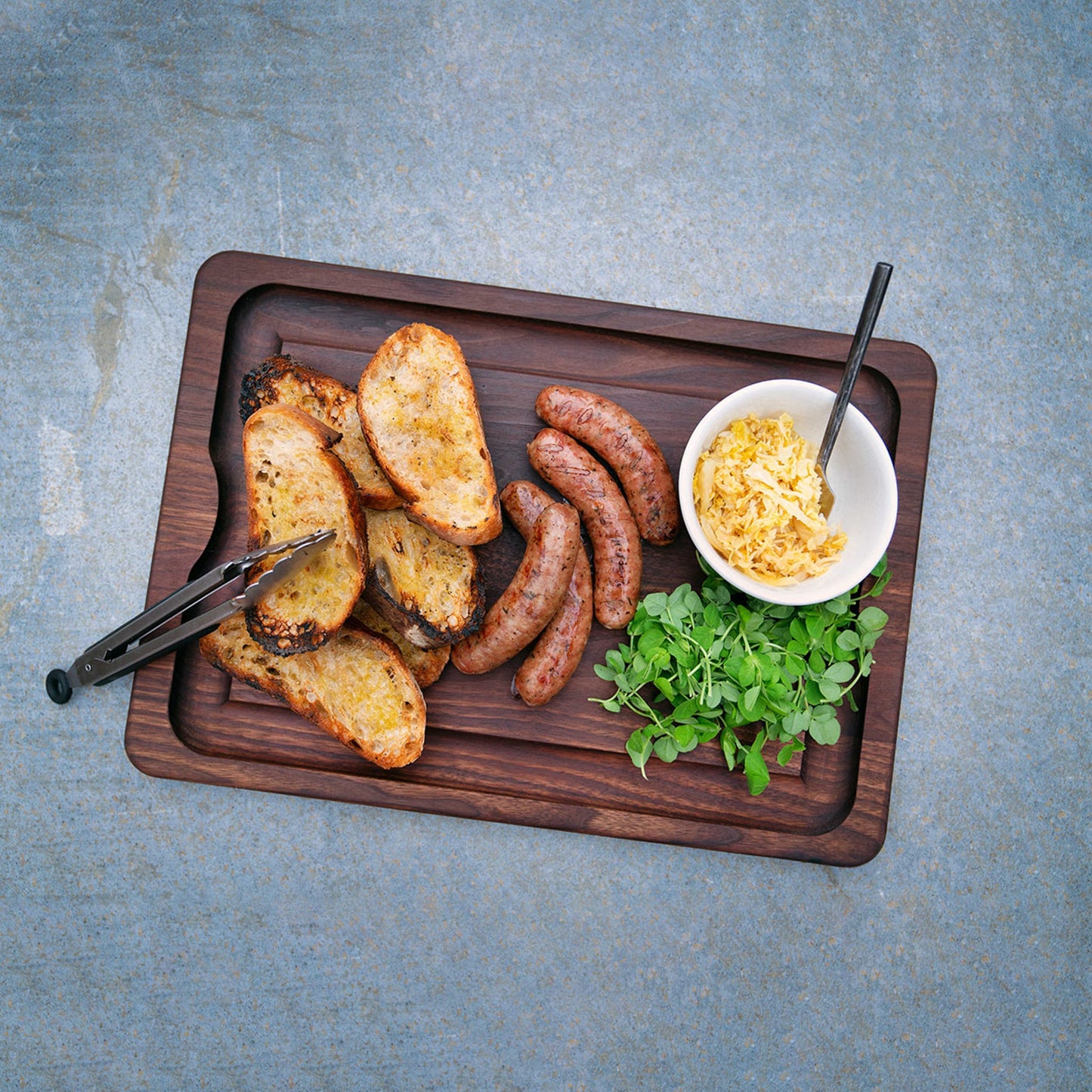 JK Adams Walnut BBQ Carving Board-20" x 14" lifestyle with grilled sausages and grilled bread.
