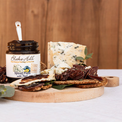 Platter of assorted cheeses, meats, and crackers with a jar of Blake Hill Spiced Plum Spread on a wooden board.