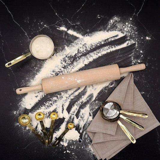 A rolling pin on a dark stone counter with flour and baking tools.  