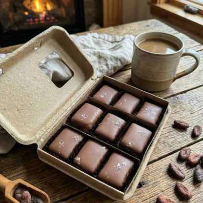 Box of chocolates on a wooden table with a cup of coffee and a fireplace in the background