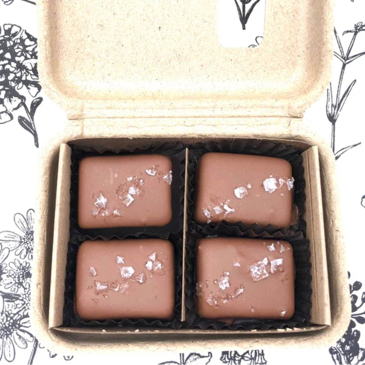 Four chocolate candies with silver flakes in a cardboard box on a floral patterned background