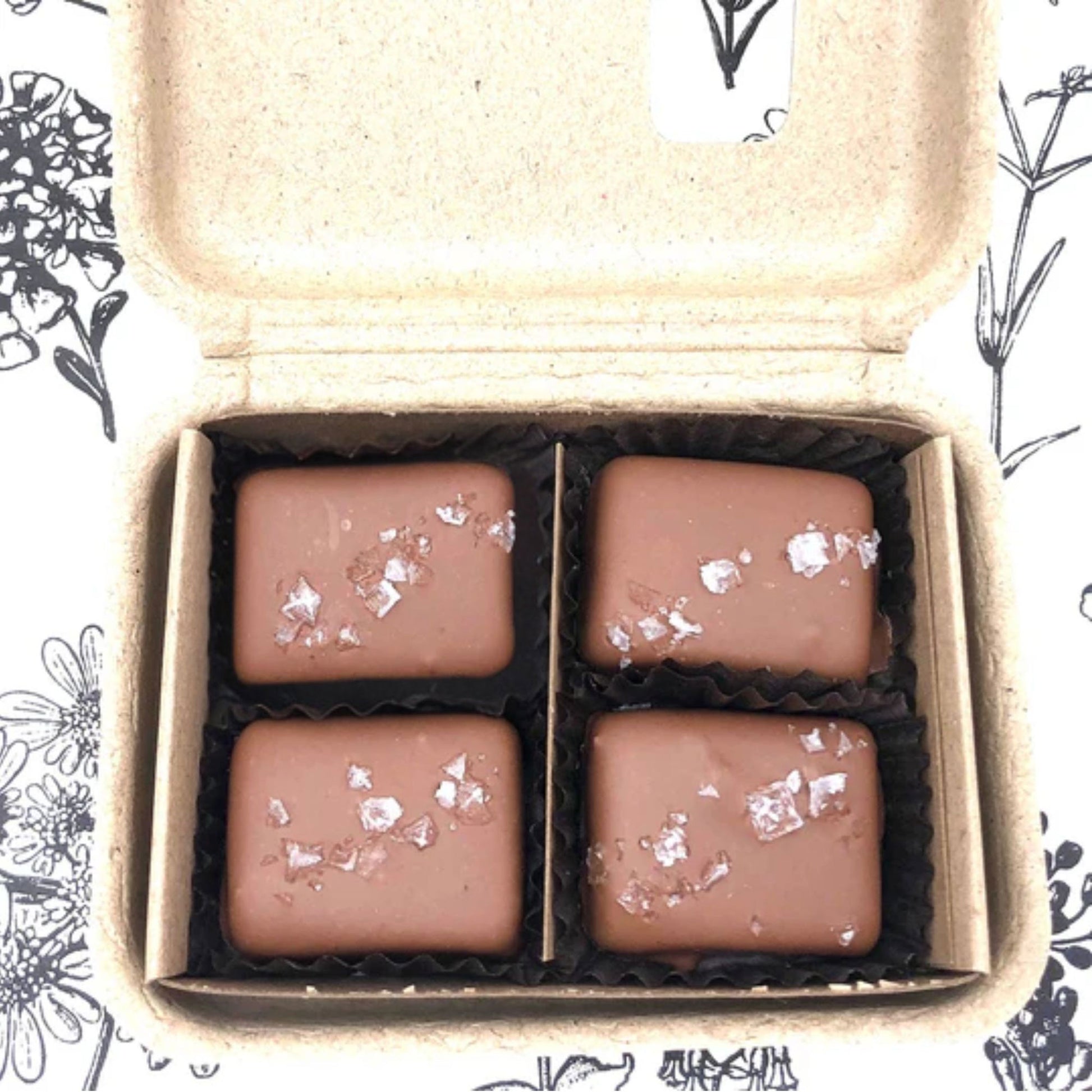 Four chocolate candies with silver flakes in a cardboard box on a floral patterned background