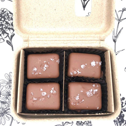 Four chocolate candies with silver flakes in a cardboard box on a floral patterned background