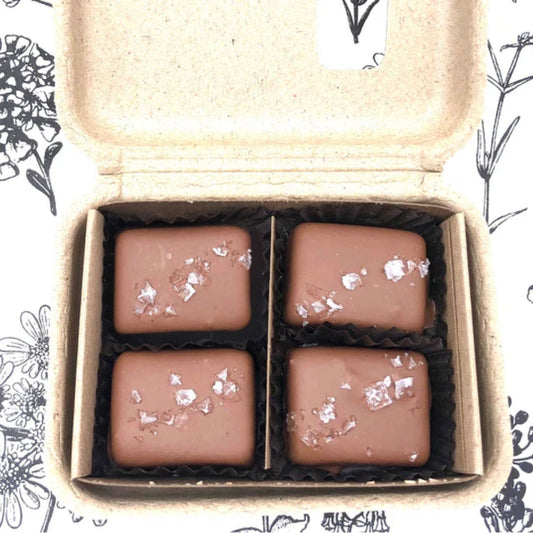 Four chocolate candies with silver flakes in a cardboard box on a floral patterned background