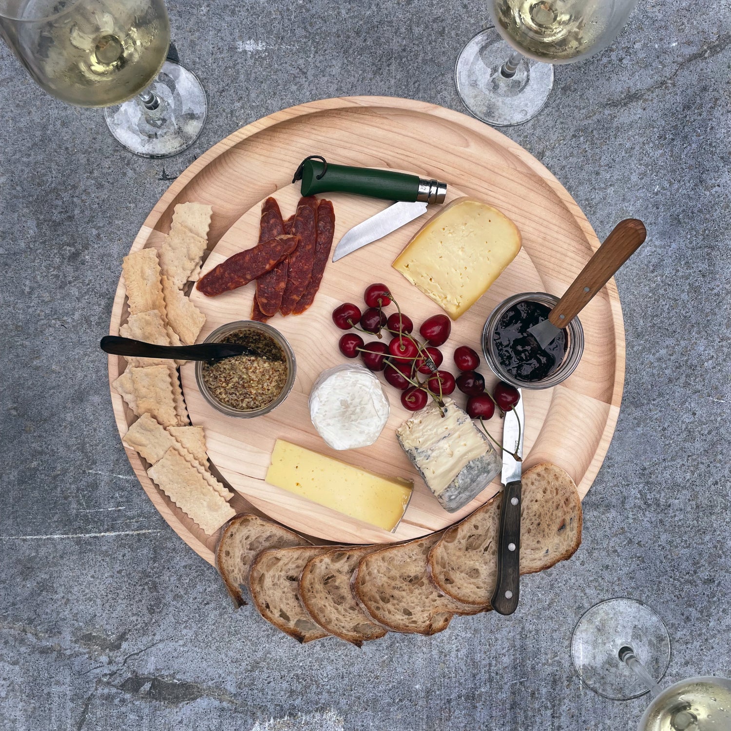 Wooden platter with assorted cheeses, meats, and bread on a stone surface.