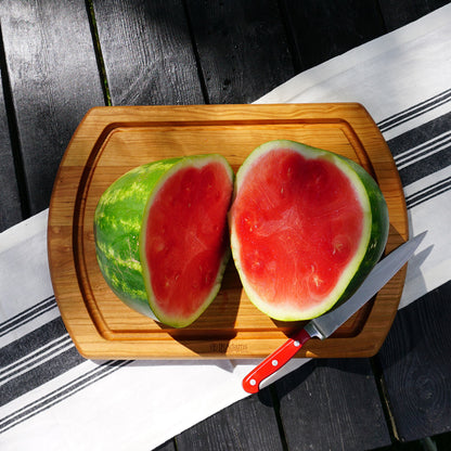 Sliced watermelon on a wooden cutting board with a knife, placed on a striped surface.