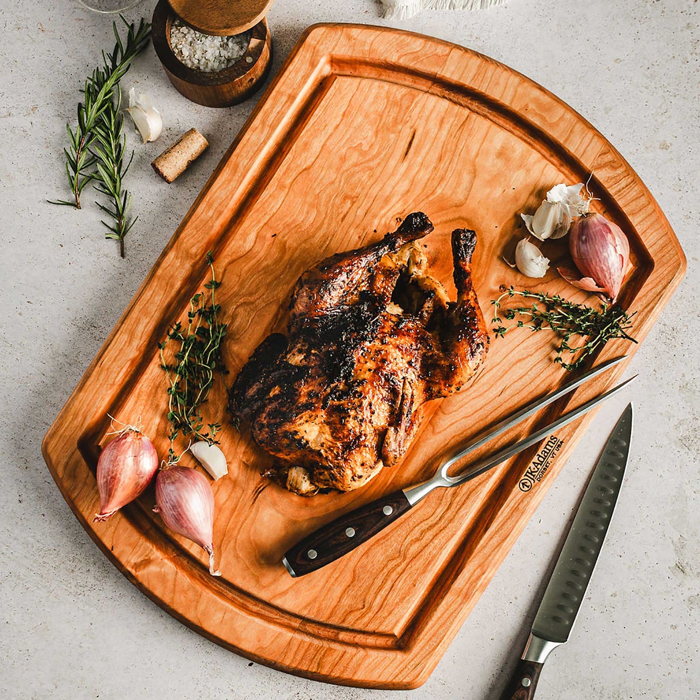Roasted chicken on a wooden cutting board with herbs and garlic, on a light gray surface.