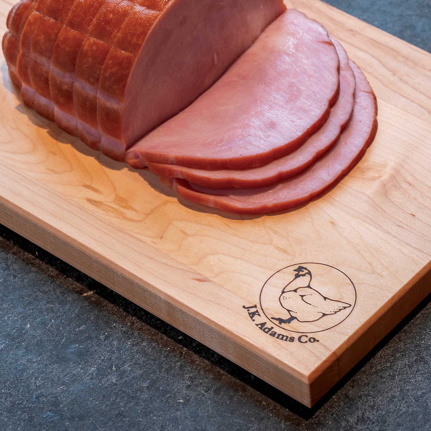 Sliced ham on a wooden cutting board with a brand logo.