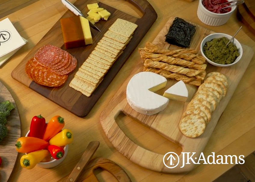Maple and Walnut serving boards with charcuterie on a maple table with the JK Adams logo in the bottom right corner. 