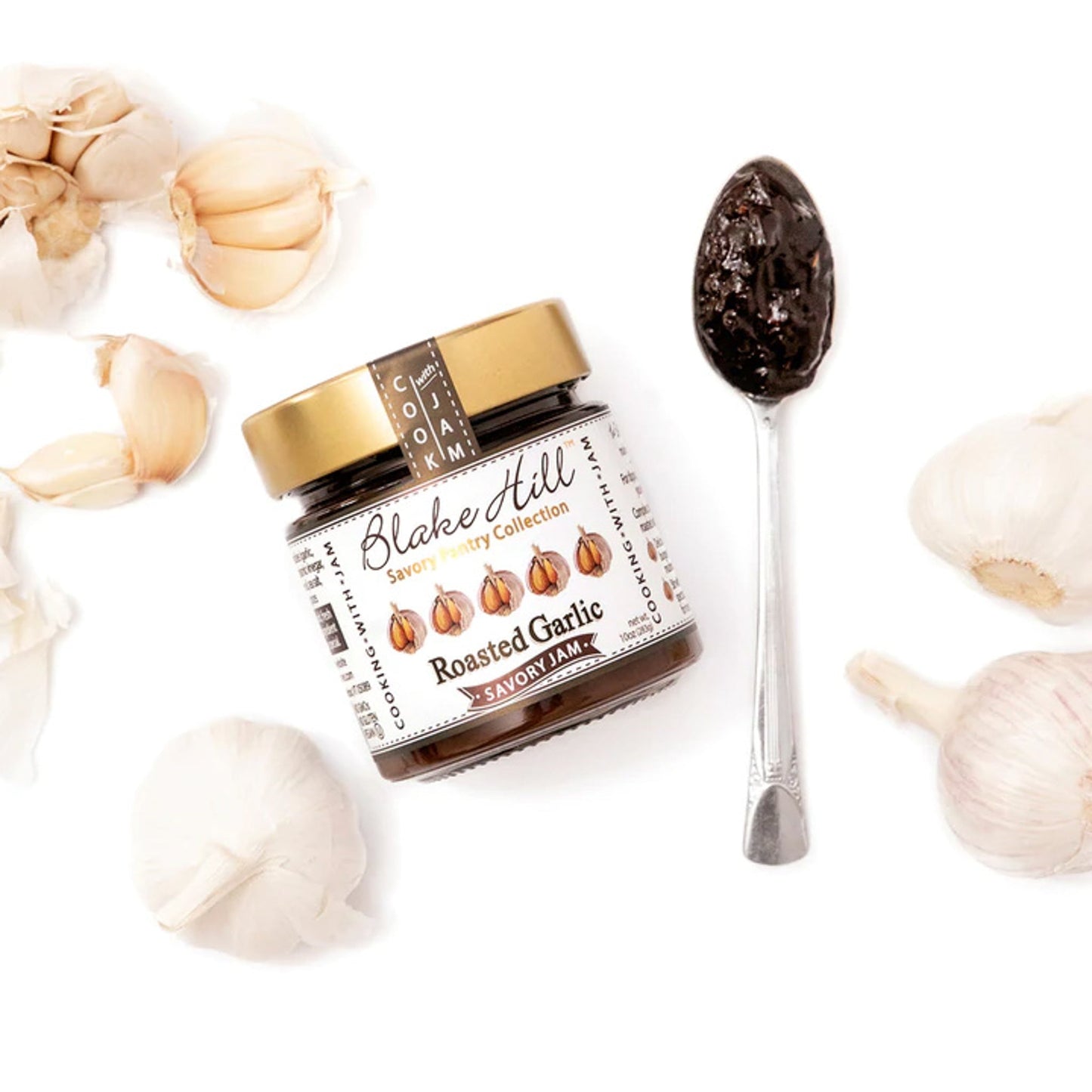 Blake Hill Roasted Garlic Savory Jam with a spoon of jam and garlic cloves and bulbs on a white background.
